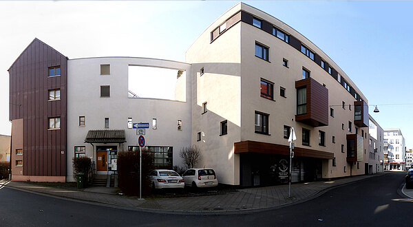 Panorama der schattigen Bettenhäuser Strasse in der neuen Unterneustadt mit hohen modernen Gebäuden. Rechts ein eckiges Gebäude mit auffälligen Erkern und  einer Änderungsschneiderei im Erdgeschoss am ehemaligen Standort des Waisenhauses. Links der unscheinbare Eingang zur neuen Kindertagesstätte.