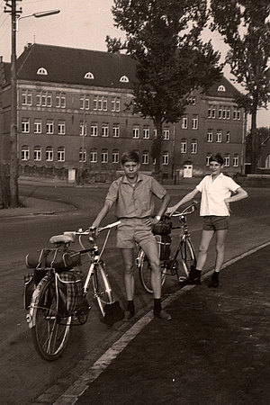 Zwei Jungen mit Fahrrad auf der Straße im Hintergrund das Schulgebäude