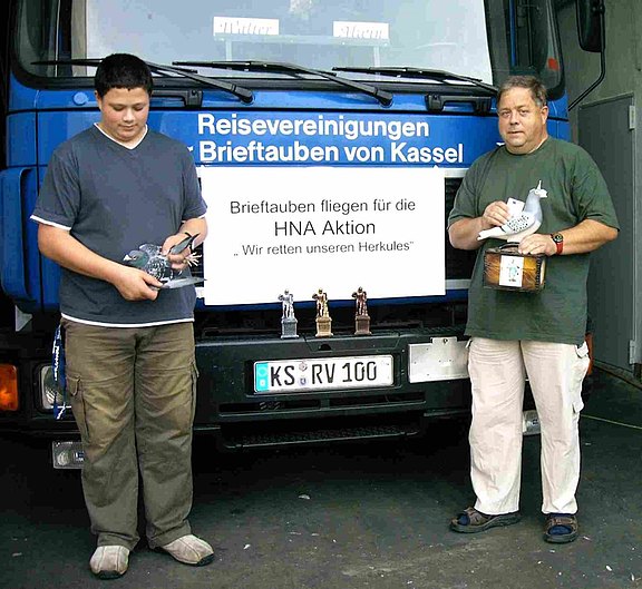 Zwei Männer mit Brieftauben in den Händen stehen vor einem Transport-LKW für Tauben 