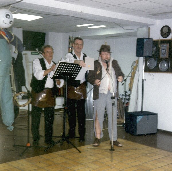 Drei Männer singen und spielen Instrumente