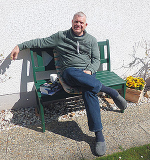Klaus-Peter Hünnerscheidt sitzt lächelnd auf einer Bank im Garten