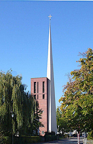 Dreieckige weise Kirchturmspitze neben rotem Glockenturm