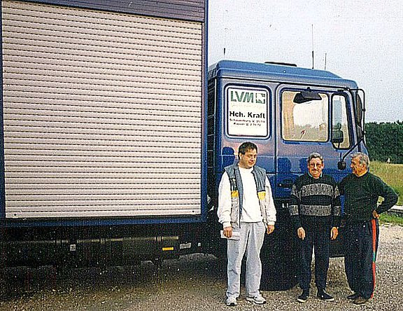 Drei Münner stehen vor dem Transport-LKW für Tauben 