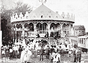 Kinder und Erwachsene stehen vor einem alten Karusell mit zwei Ebenen von Schellberg, 1906