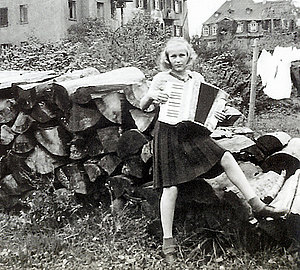 Maedchen Rosemarie mit Akkordeon vor Holzstoss, 1950