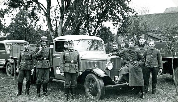 Fertig zur erzwungenen Übergabe an das Militär in einem Garten. Mehere Personen in Uniform, dritte Person von links Hans Hess. 