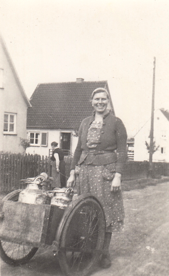 Elisabeth Jetzizack beim Milch ausfahren mit Stoßkarren auf dem Milchkannen stehen 