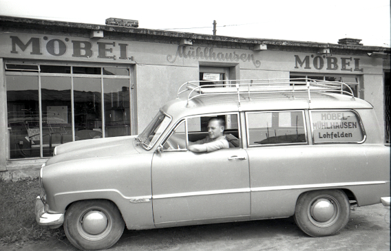 Gerhard Mühlhausen im Ford Kombi vor dem Möbelladen in einer Kriegsbaracke