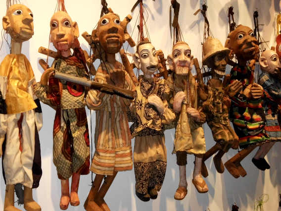 Viele Holz-Marionetten hängen vor einer weissen Leinwand 
