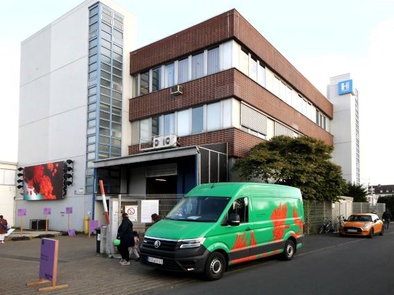 Ein grüner Kleintransport der d15 steht vor dem Ausstellungsgebäude der Firma Hübner, Besucher gehen aus Gelände 