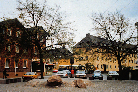 Blick auf Springbrunnen am Leipziger Platz, dahinter die Häuser Dormannweg 7-9 und parkende Autos 