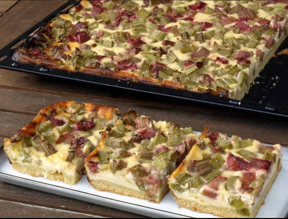 Rhababerkuchen auf einem Blech, davor drei Stücke geschnitten mit Schmand 