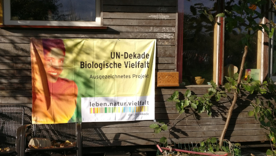Plakat UN Dekade Biologische Vielfalt vor Gartenhütte 