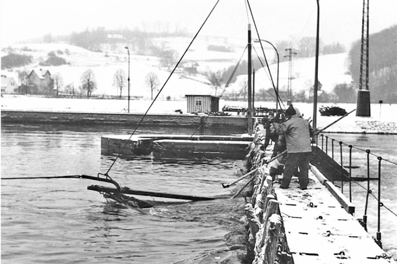 Winterarbeiten an der Schleuse Wolfsanger. Männer versuchen mit Stangen etwas aus dem Wasser zu holen. 